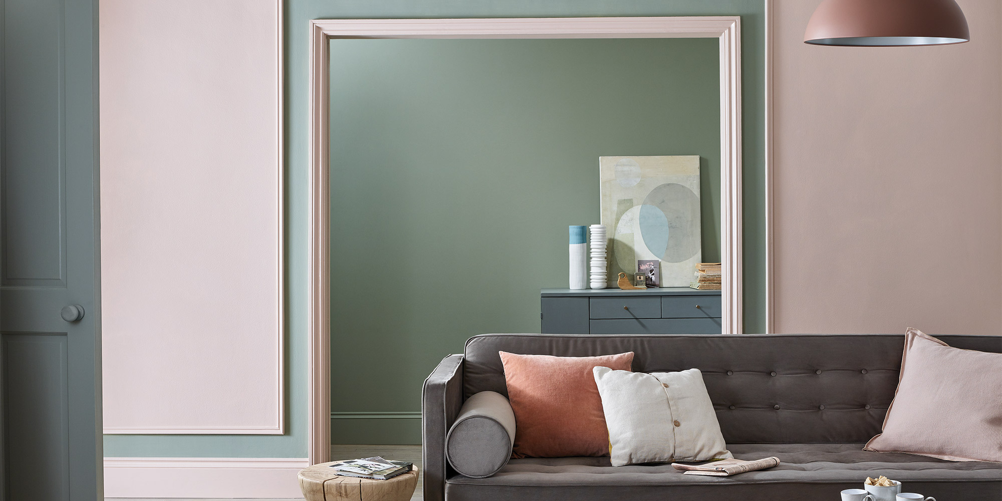 Wohnraum mit breitem Durchgang und weißer Türzarge, davor graues Sofa mit Kissen