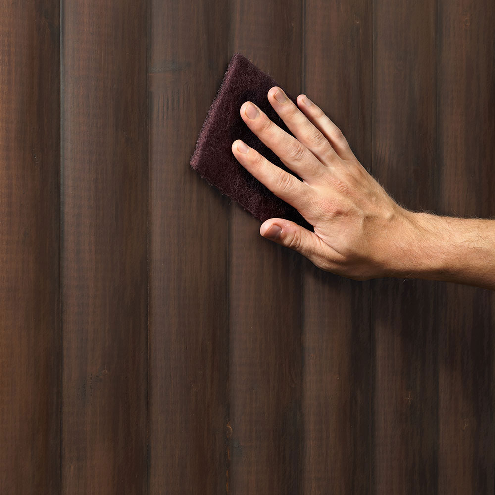 Hand schleift dunkle Holzoberfläche mit Schleifpad als Vorbereitung für die Aufhelltechnik