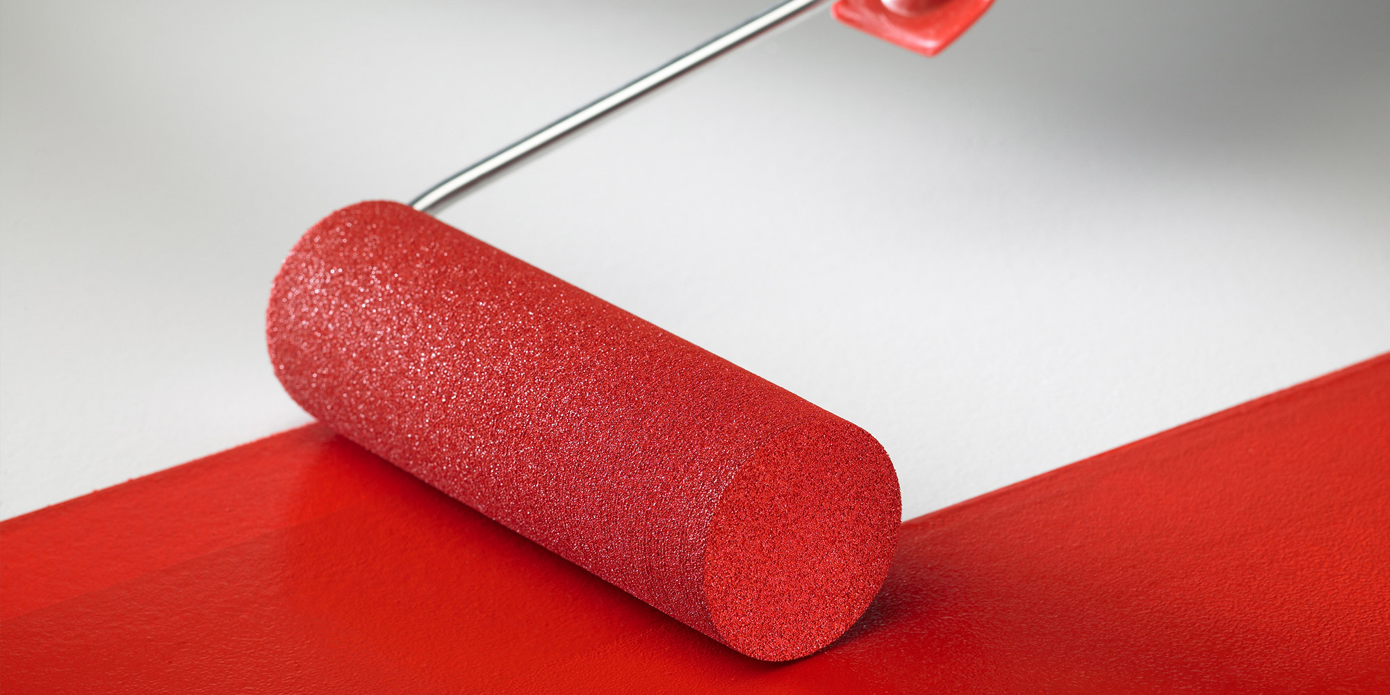 Schaumrolle verteilt roten Lack auf glatter Oberfläche, gleichmäßiger Farbauftrag