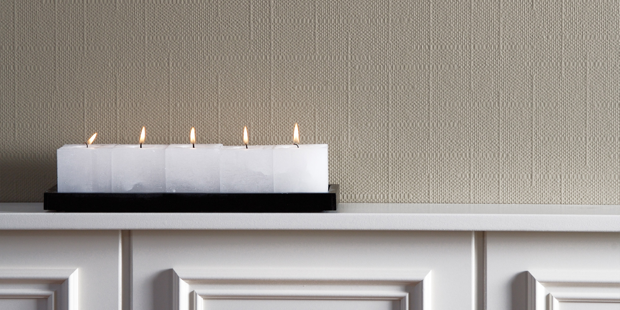 Kerzen auf Ablage vor strukturierter Wandoberfläche aus Gewebe