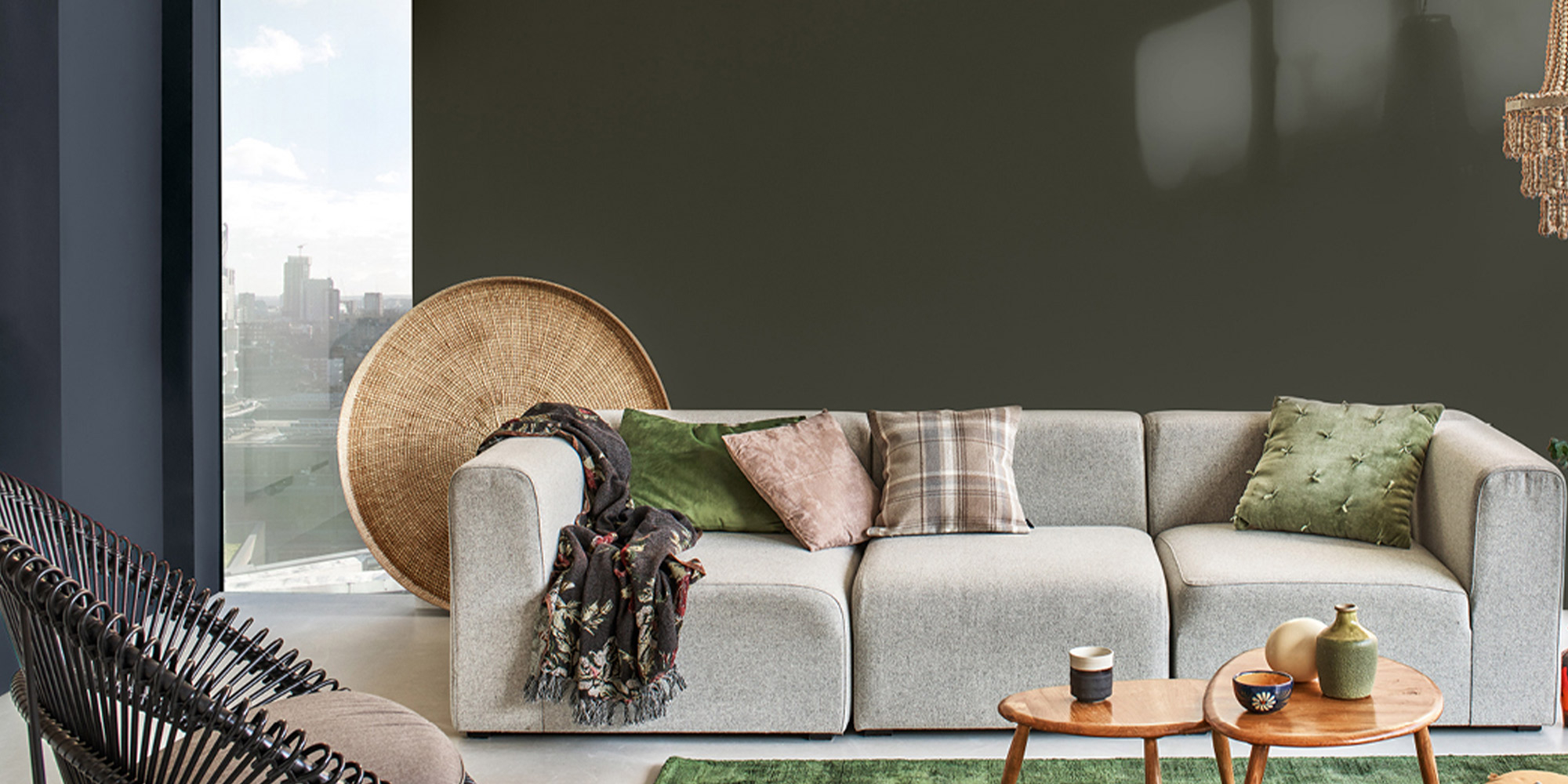 Wohnzimmer mit dunkelgruener Wand, grauem Sofa, Kissen und kleinen Holztischen als Farbbeispiel
