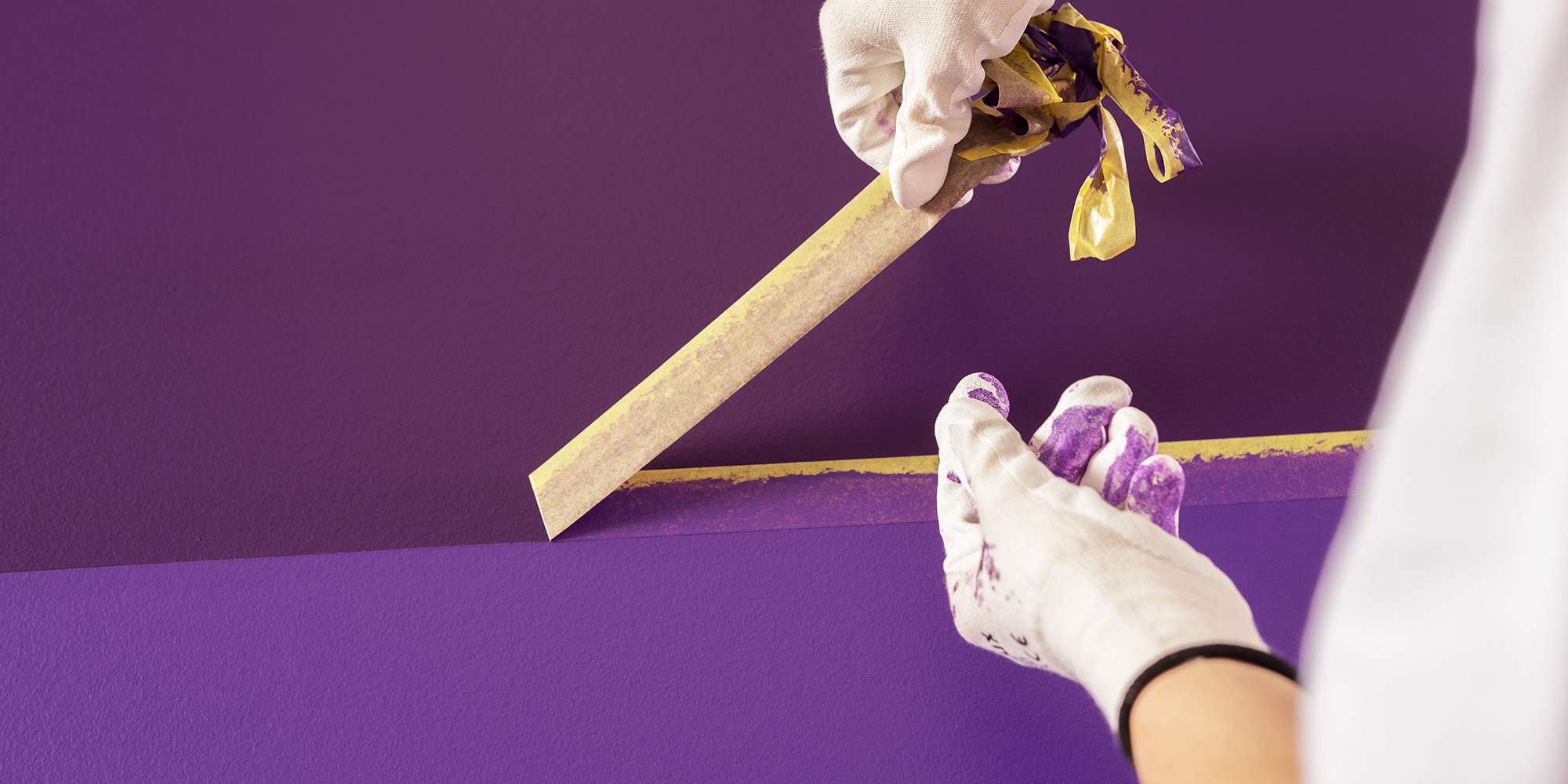 Handschuhe kleben Abdeckband auf eine violette Wand fuer eine saubere Farbkante