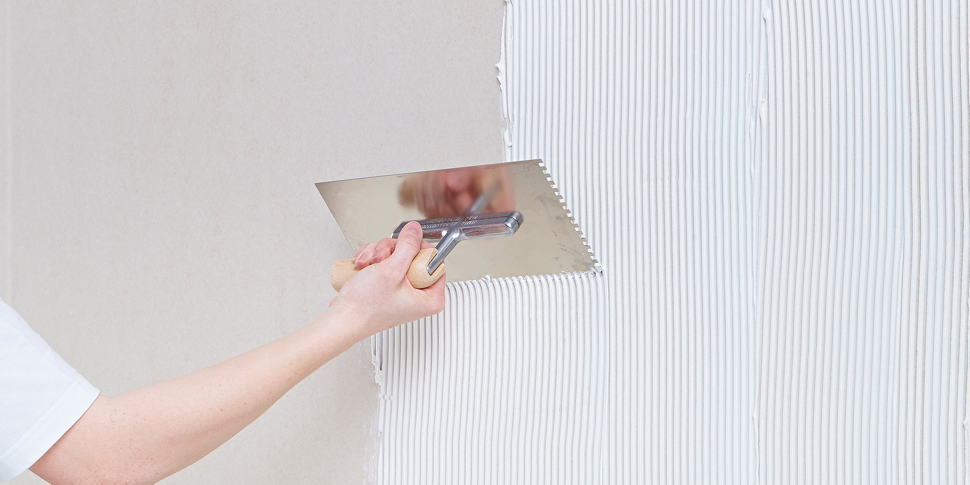 Person glättet Spachtelmasse mit Kelle auf der Wand, gleichmäßige Struktur entsteht