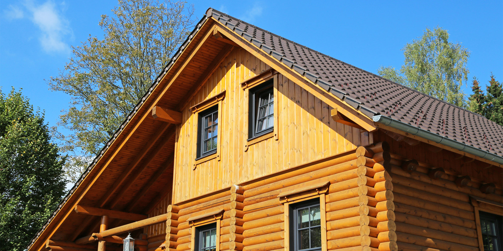 Blockhaus aus Rundholz mit Satteldach und Fenstern vor blauem Himmel