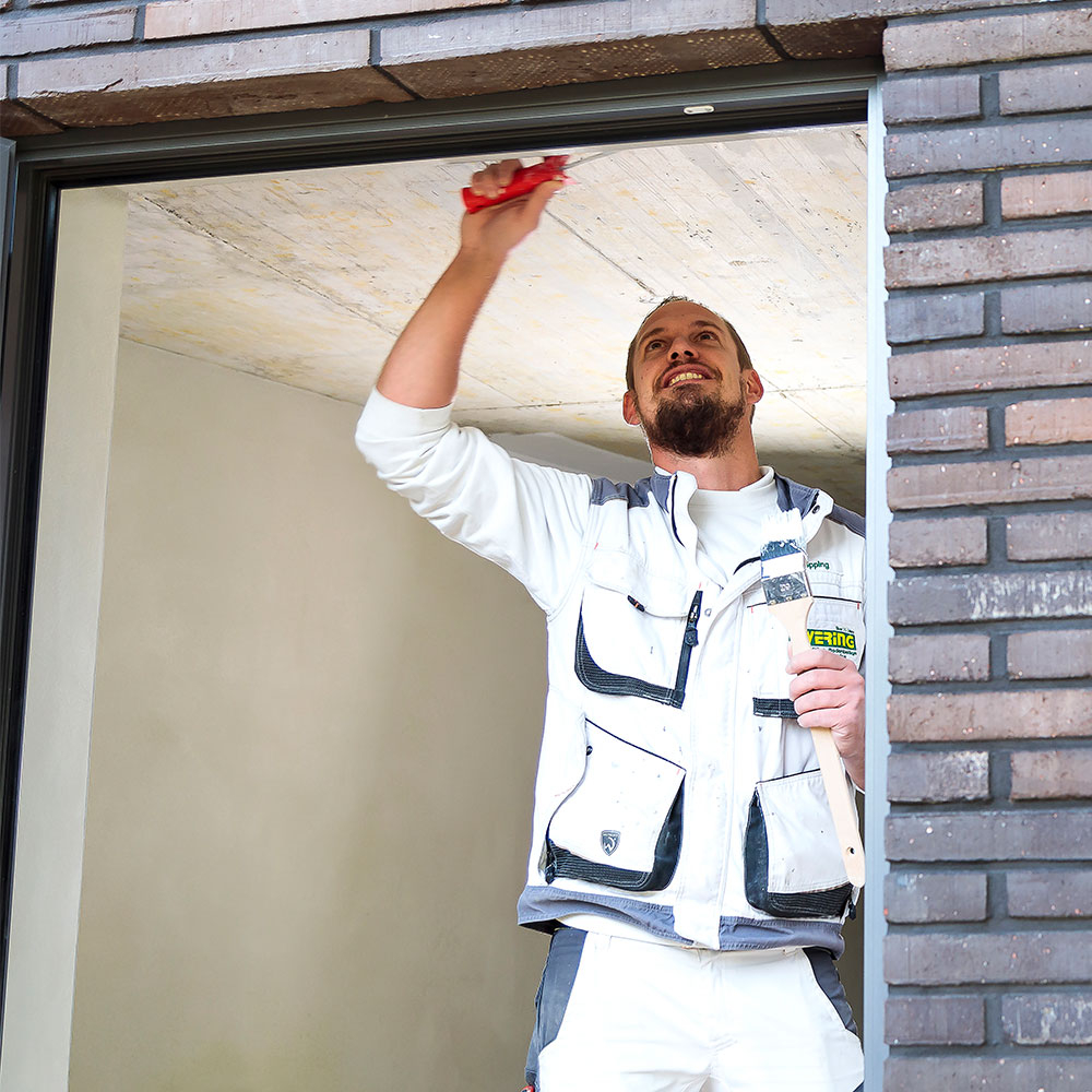 Maler im Fensterbereich kratzt und reinigt die obere Kante, Untergrundvorbereitung fuer Aussenlack