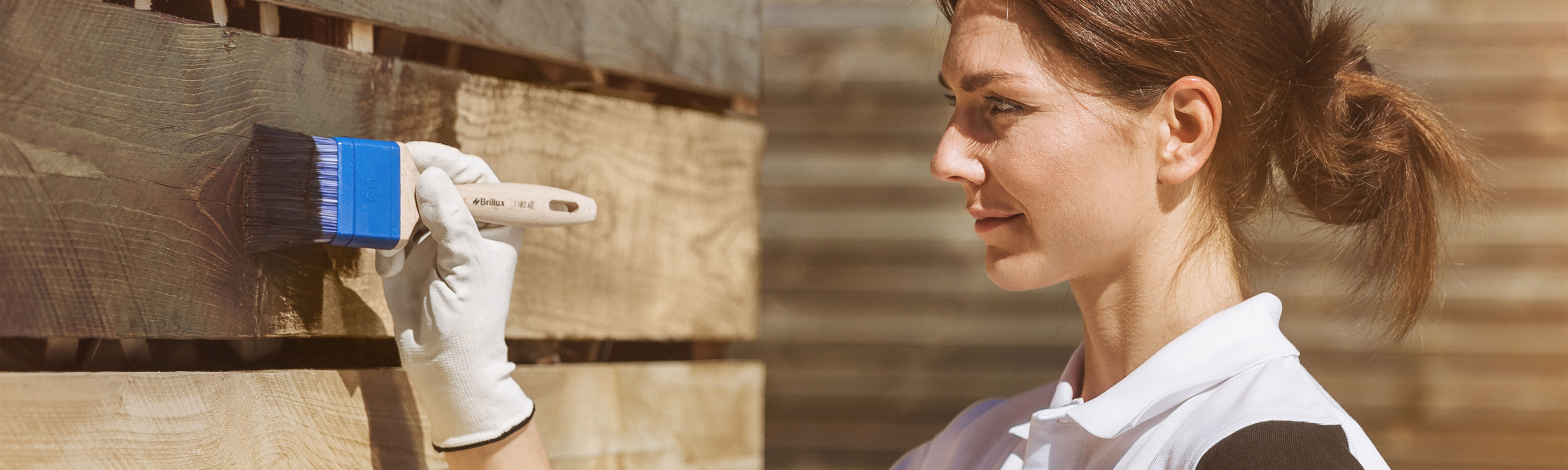 Malerin trägt Holzschutz mit Pinsel auf Holzzaun auf - Beispiel für Vorbereitung vor dem Streichen eines Holzzauns