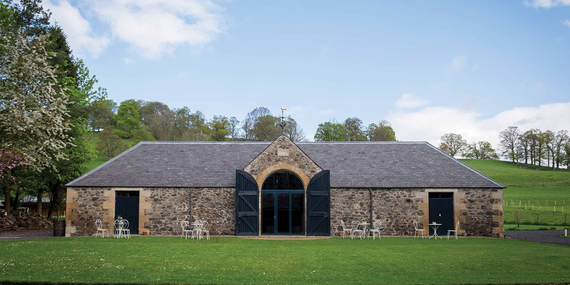 Historisches Steingebäude mit dunklen Toren, Sitzgruppen und großer Rasenfläche