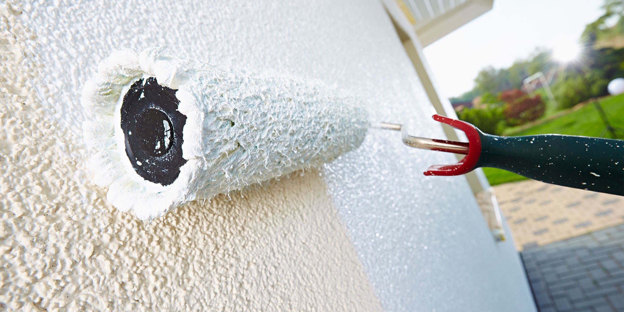 Farbroller traegt weisse Fassadenfarbe auf rauen Putz auf - gleichmaessiger Schutzanstrich fuer die Hauswand