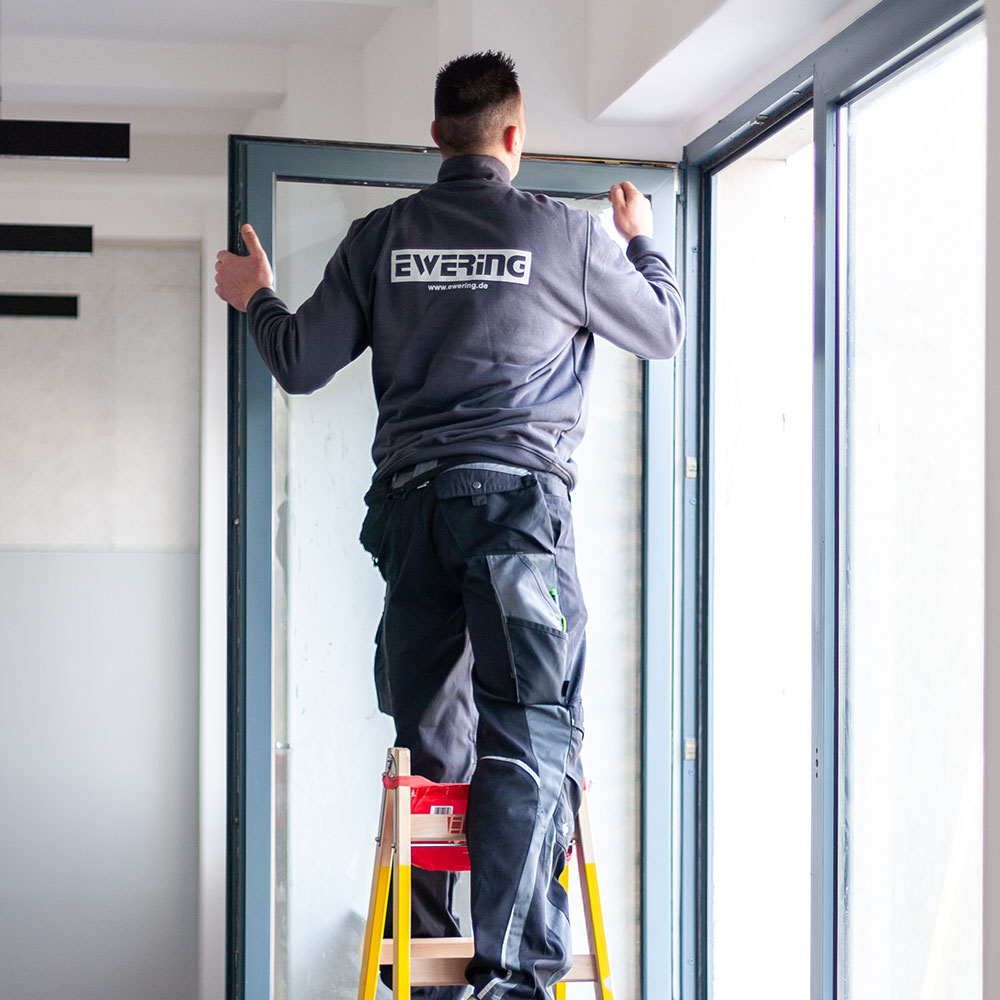 Handwerker auf Leiter setzt Fensterelement ein, Vorbereitung vor dem Lackieren von Rahmen und Fluegel