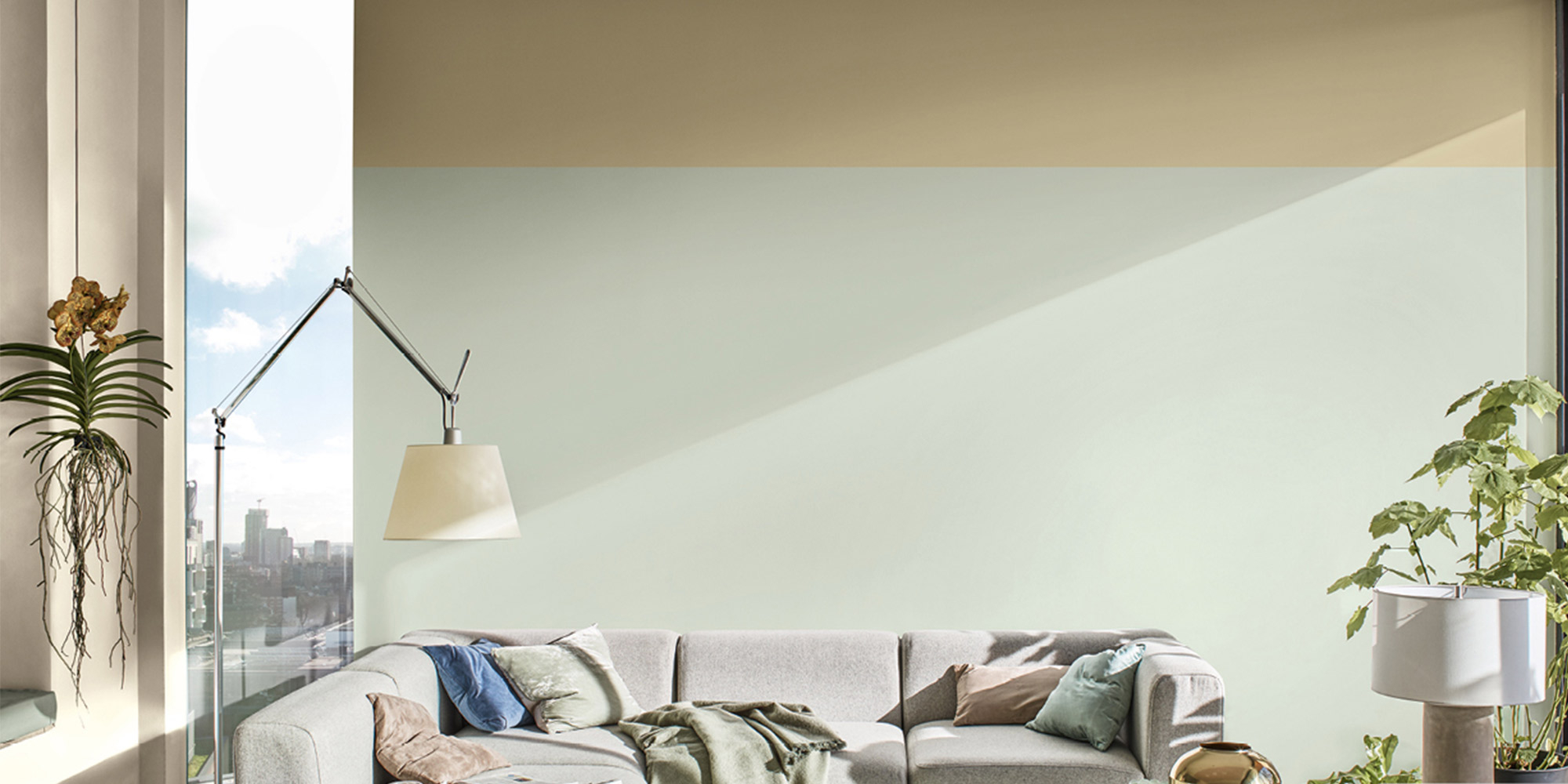 Helles Wohnzimmer mit zweifarbiger Wand in Beige und Mintgruen, helles Sofa und Stehleuchte am Fenster