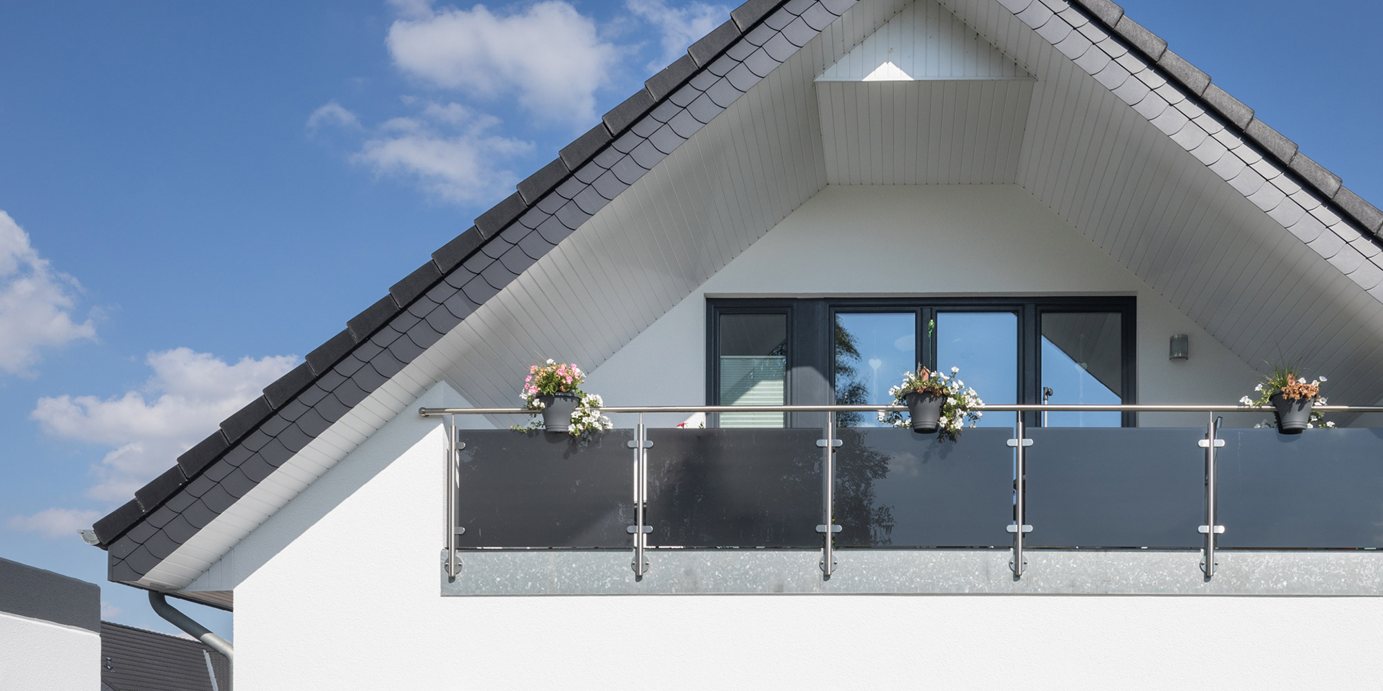 Hausfassade mit Dachüberstand und Balkon mit Blumenkästen unter blauem Himmel