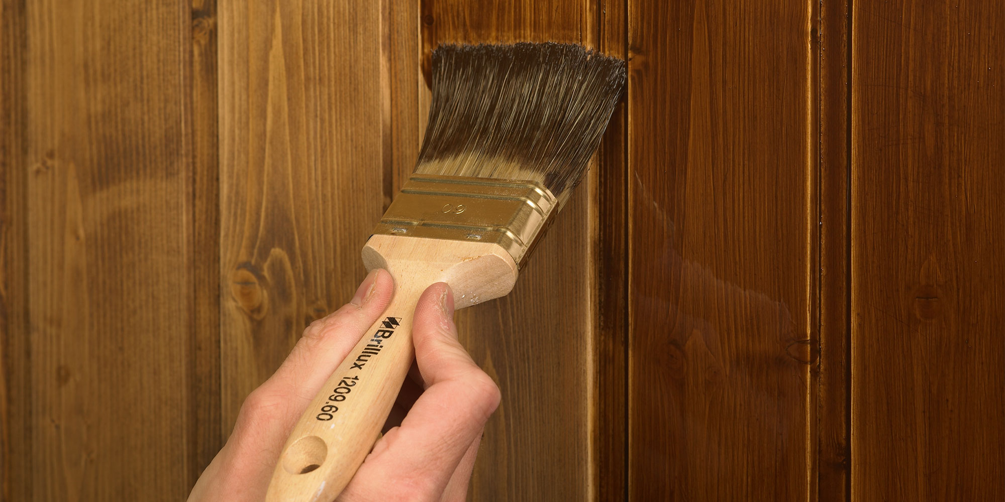 Pinsel traegt dunkle Lasur auf Holzbrett auf - Beispiel fuer FAQ zur Lasur Verarbeitung