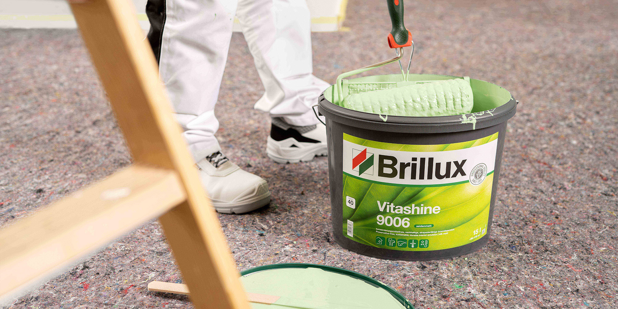 Farbrolle liegt in einem Eimer mit gruener Farbe zum Streichen
