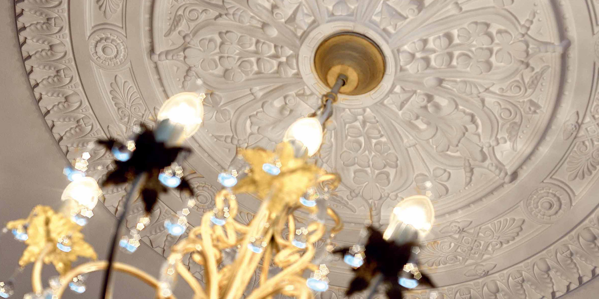 Große dekorativ verzierte Stuckrosetten gestalten optische Highlights in einem exklusiven Wohnzimmer.