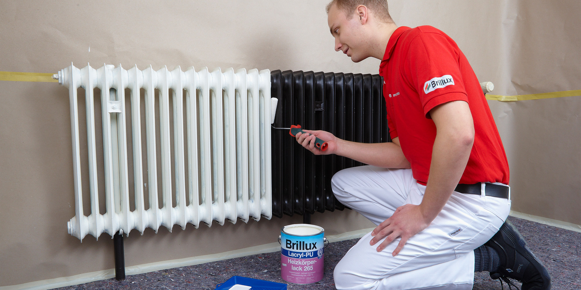 Maler lackiert einen Heizkörper mit Rolle, Brillux Heizkörperlack Dose steht daneben