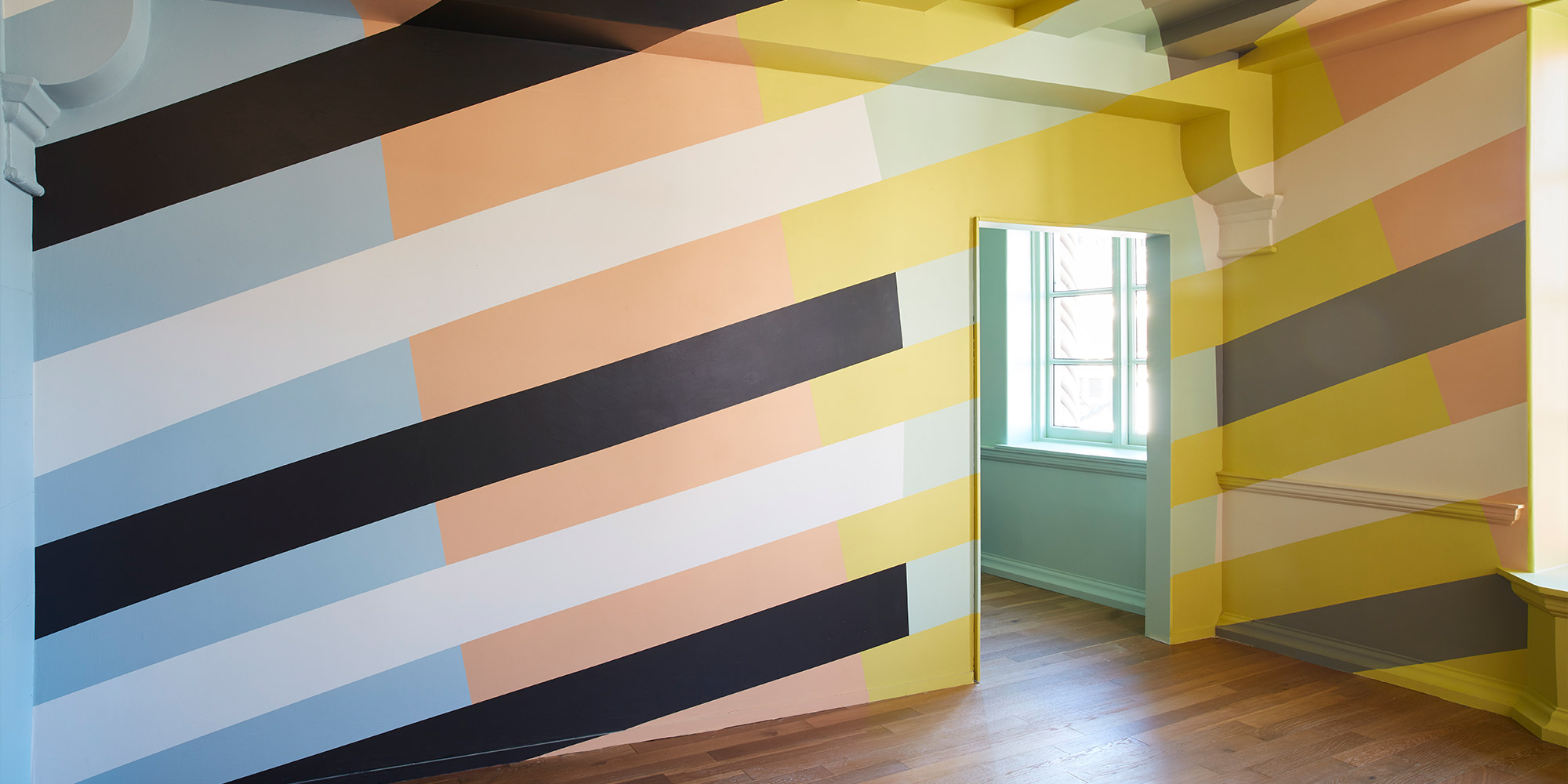Wandgestaltung mit breiten diagonalen Streifen in Blau, Gelb, Weiß und Schwarz