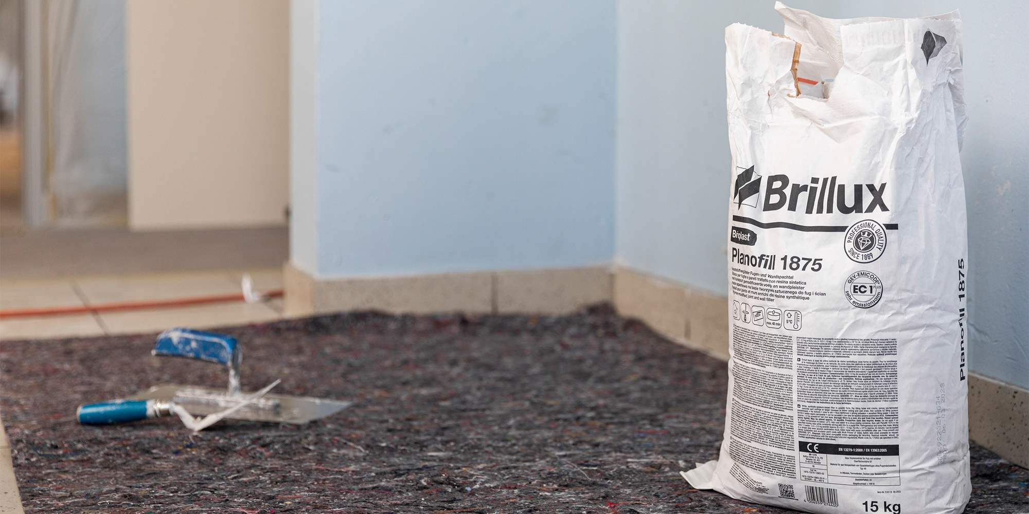 Sack Brillux Planofill 1875 im Renovierungsraum, Spachtelwerkzeuge liegen auf dem Boden