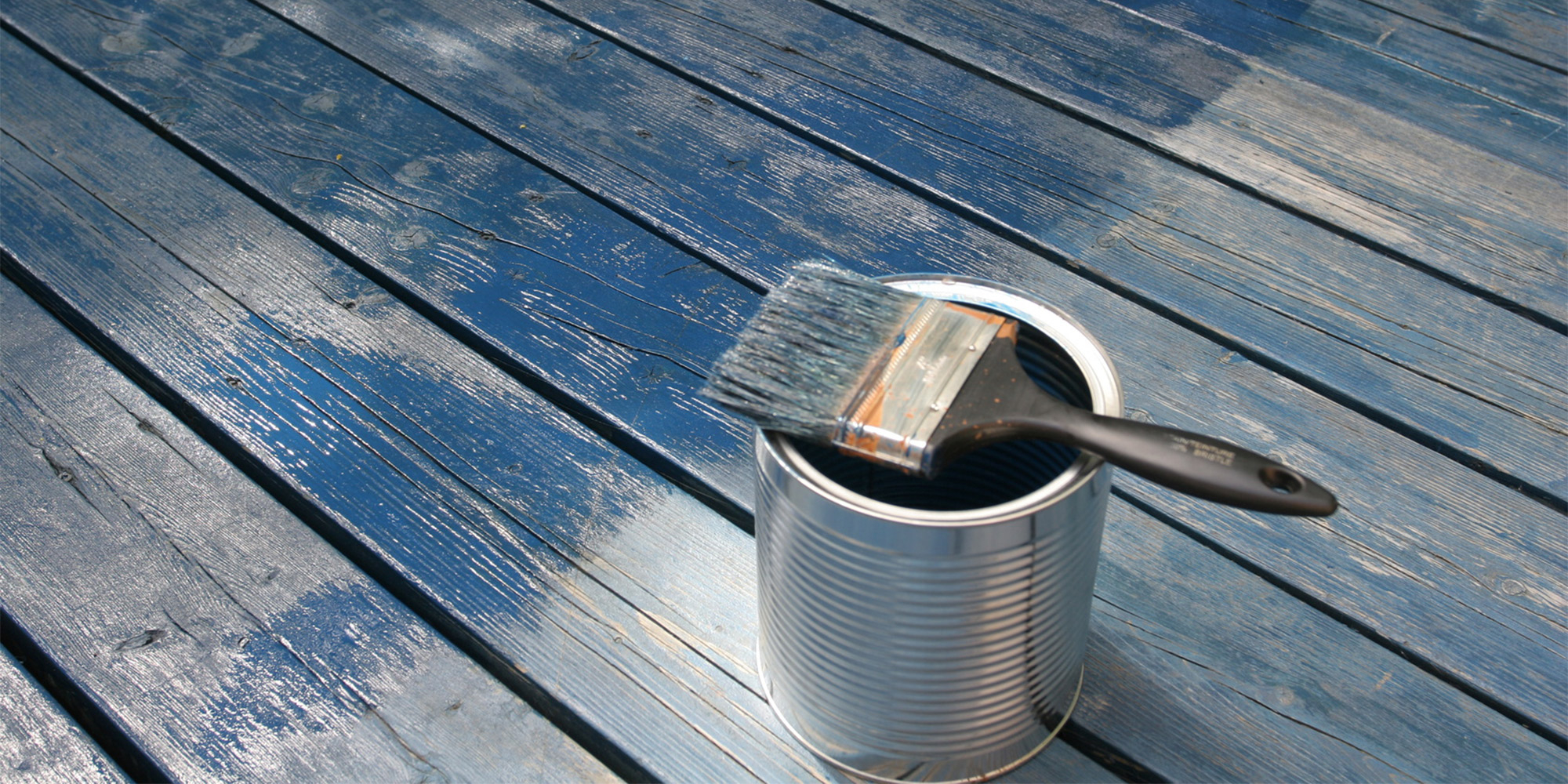 Schwarzer Pinsel liegt auf einer offenen Farbdose auf blau gestrichenen Holzdielen, frischer Anstrich sichtbar