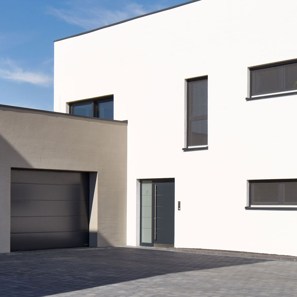 Modernes Haus mit weißer Fassade, grauer Garage und dunkler Metall Haustür - Beispiel für Anstrich und Pflege