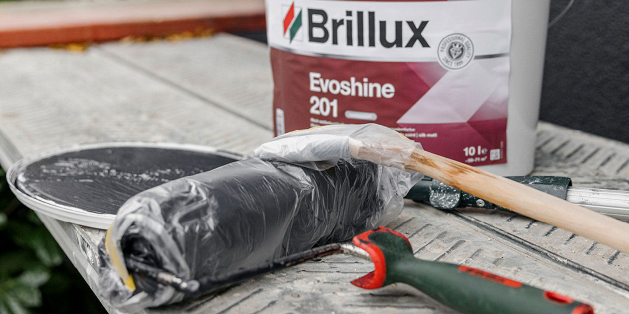 Farbroller in Folie auf Geruest, daneben Brillux Evoshine 201 - Vorbereitung fuer den Fassadenanstrich