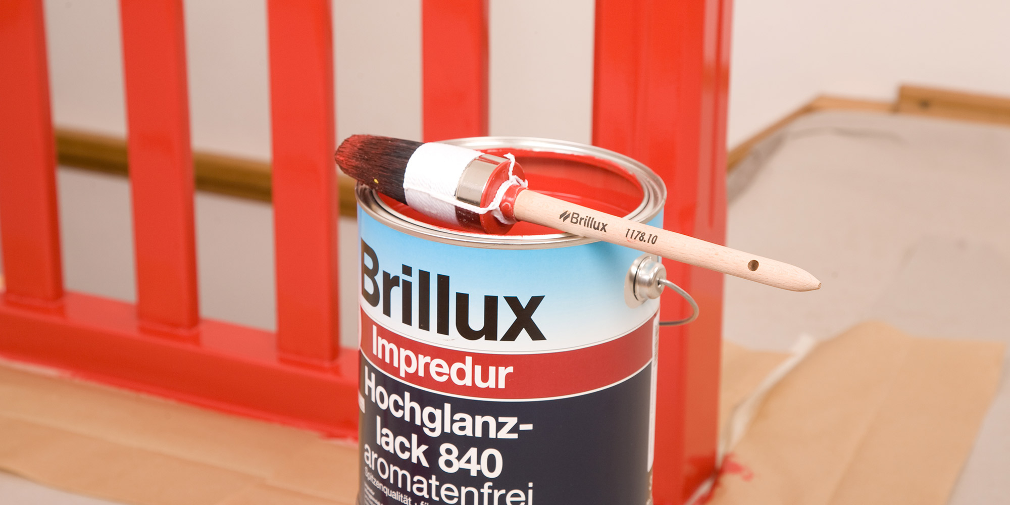 Pinsel auf rotem Lacktopf vor gestrichenem Geländer, Motiv für Vorlacke