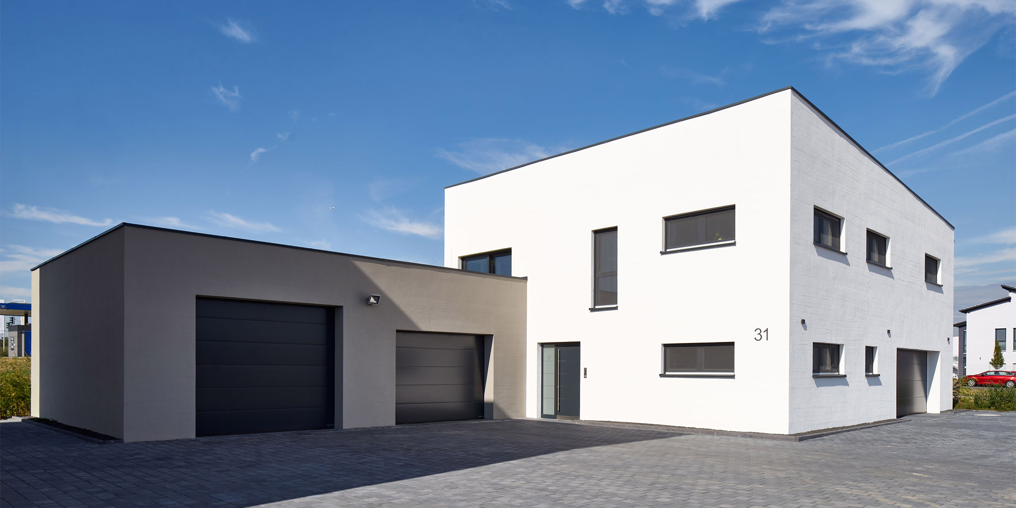 Modernes Wohnhaus mit heller Fassade und dunkler Garage, Beispiel für Fassadenbeschichtung