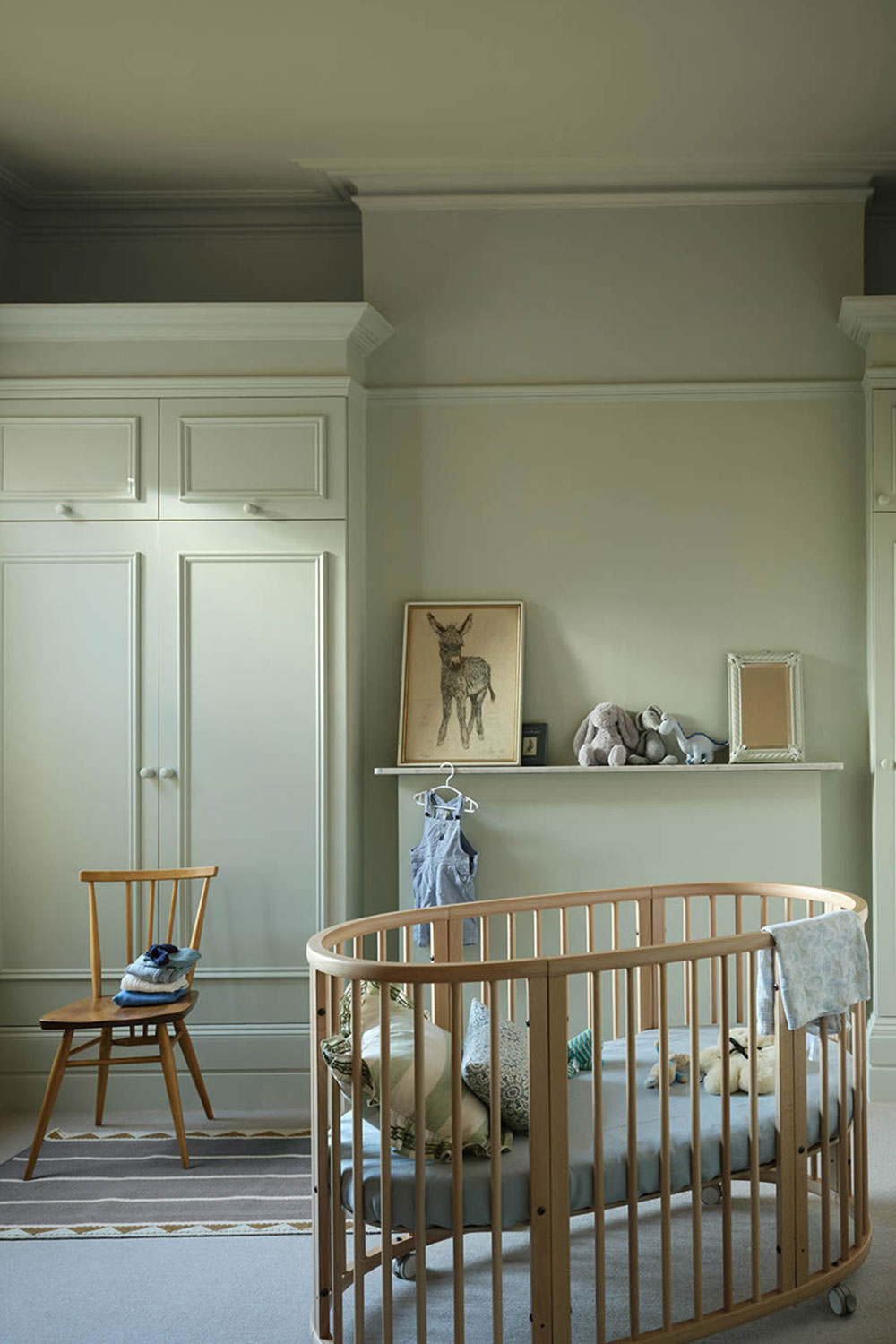 Helles Kinderzimmer mit rundem Babybett und weiß lackierten Einbauschränken in sanftem Graugrün