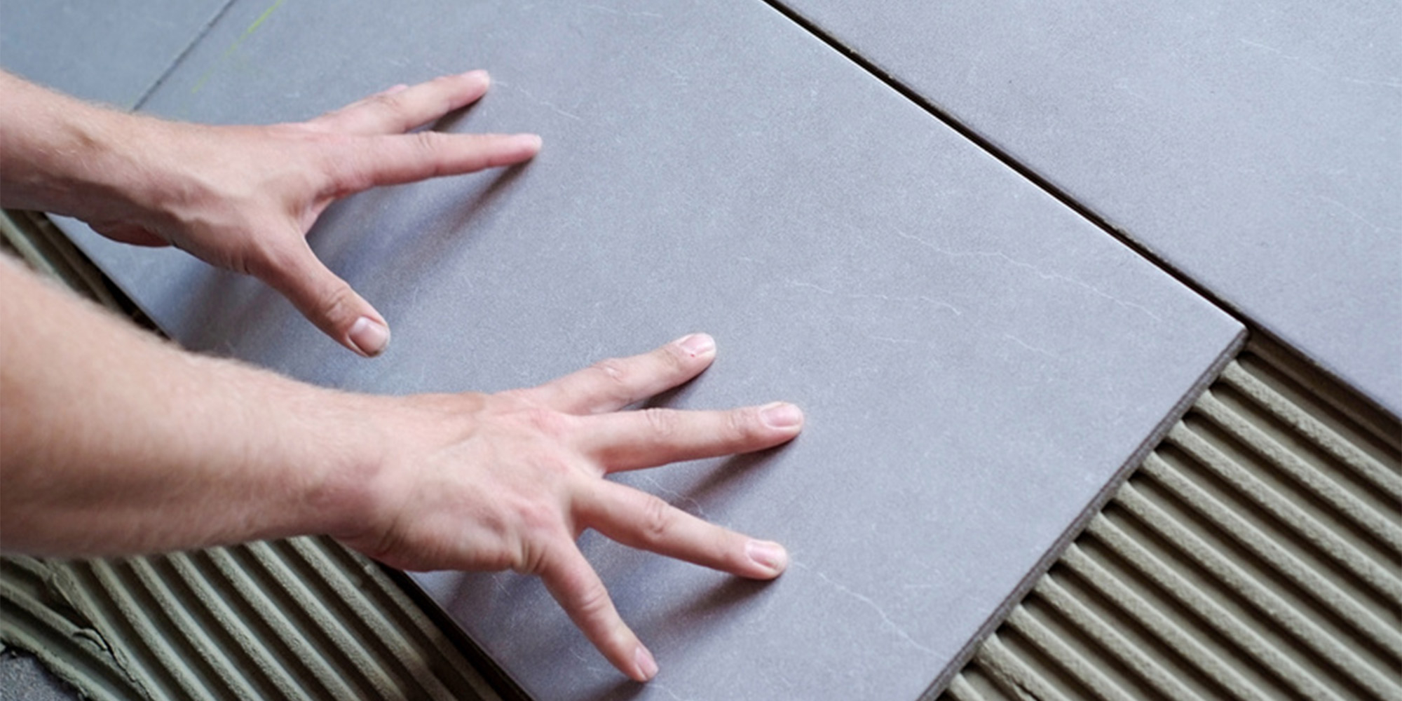 Haende richten grosse Fliesen im Kleberbett aus und druecken sie an