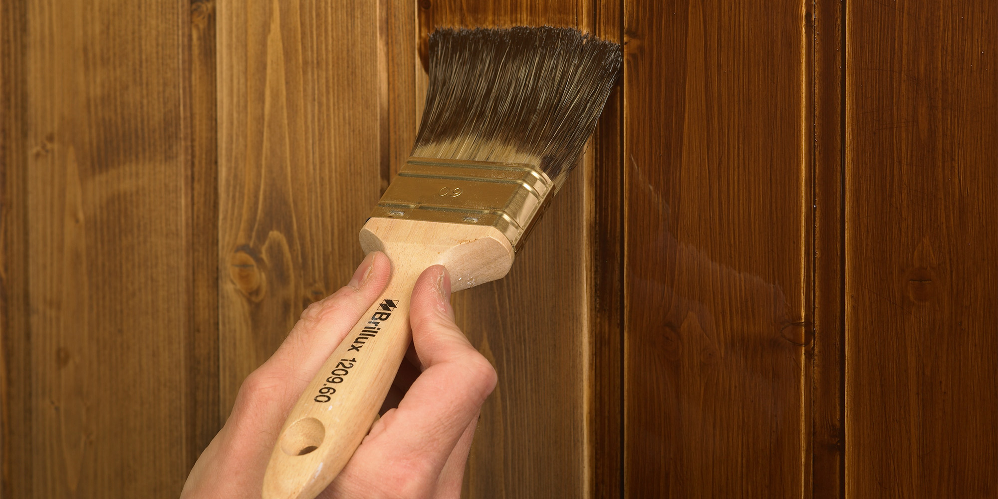 Pinsel traegt Holzlasur gleichmaessig auf eine Holzoberflaeche auf