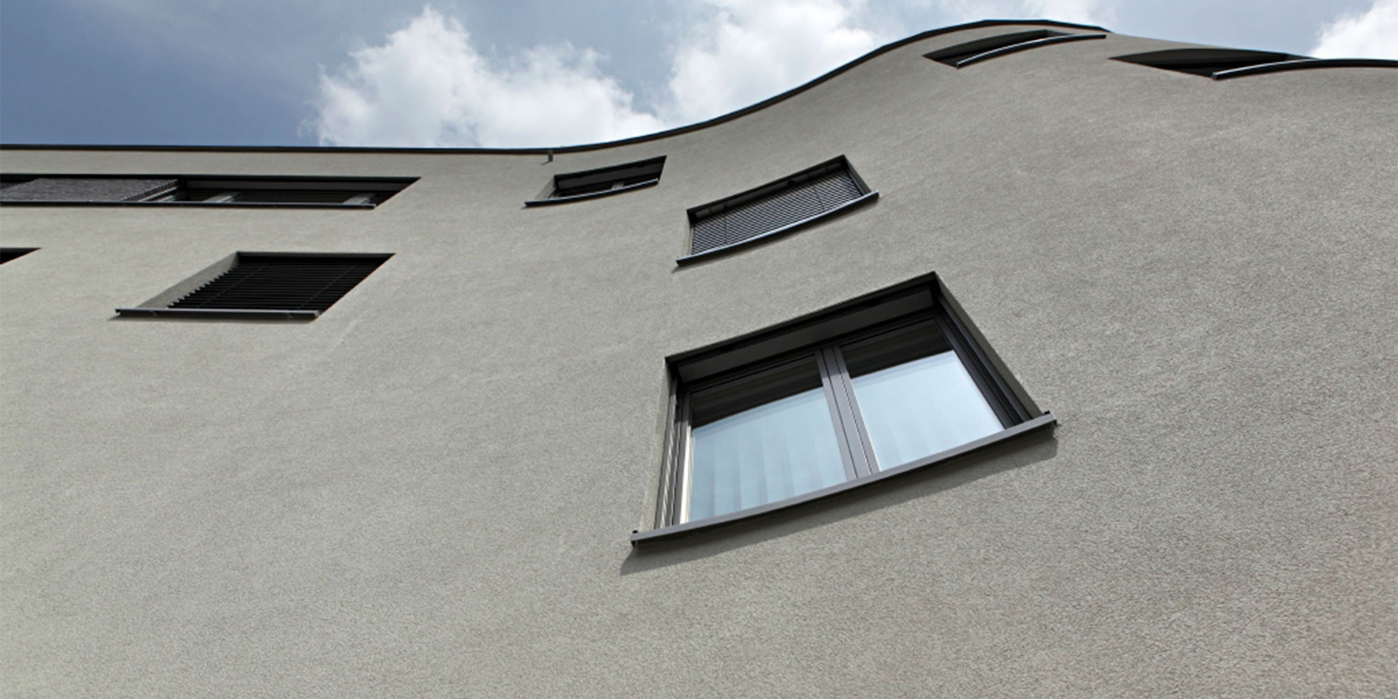 Untersicht auf eine geschwungene Rausanputz Fassade mit Fenstern und gleichmäßiger Struktur