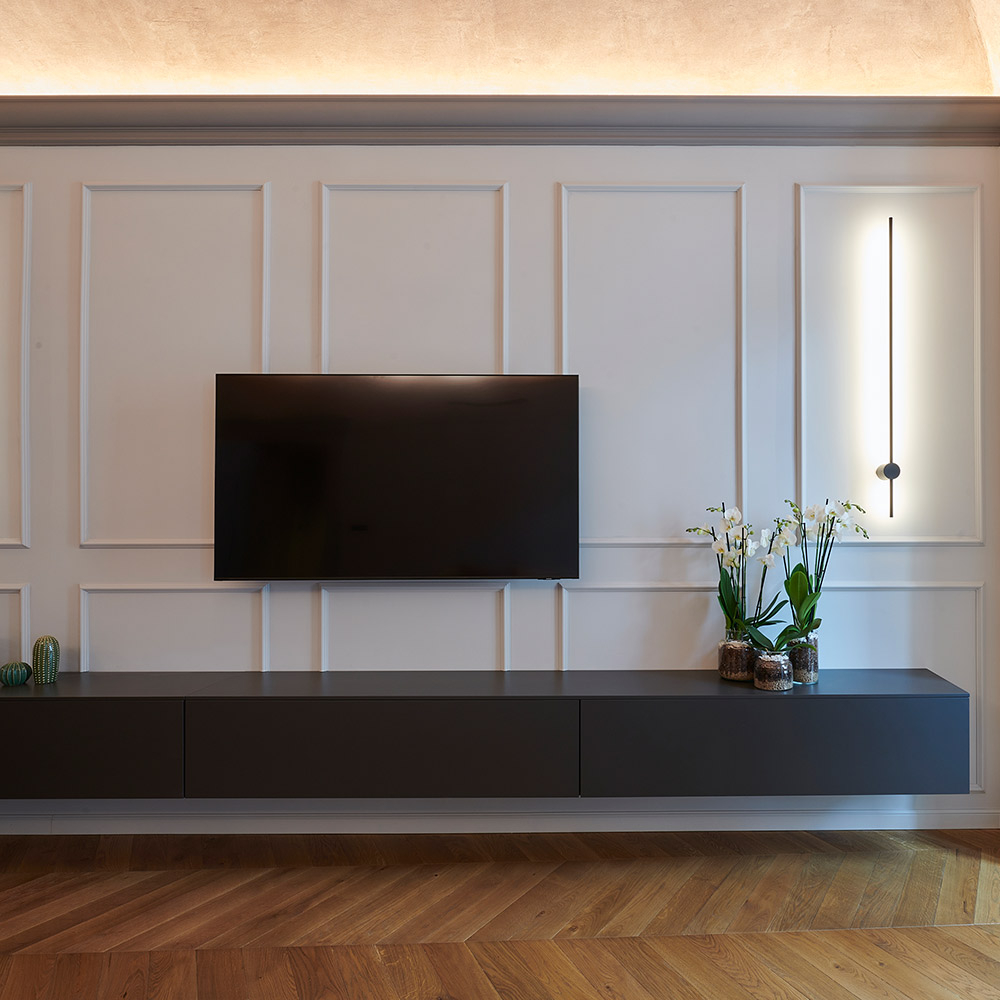 Wandgestaltung hinter dem Tv-Board im Wohnzimmer mit stilvollen Wandfeldern aus schmalen Stuckleisten.