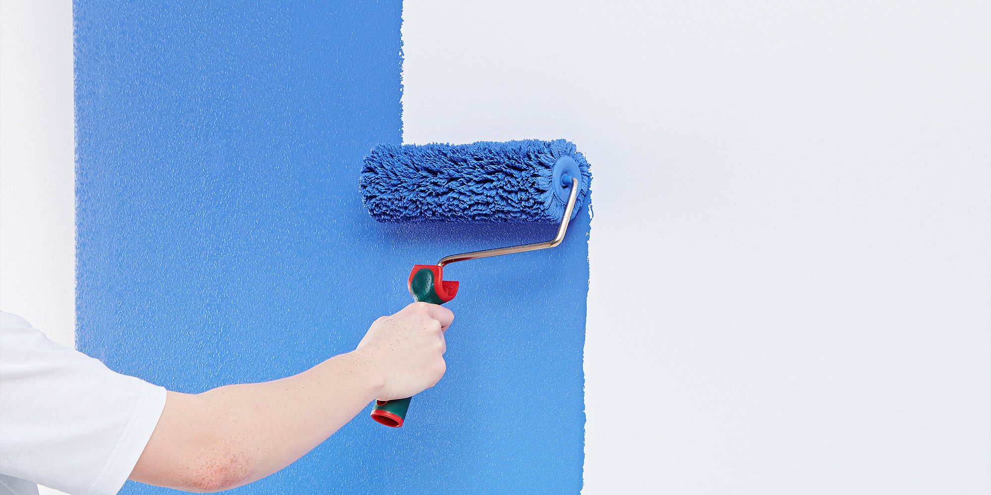 Maler rollt blaue Innenfarbe auf eine Wand für ein gleichmäßiges Finish