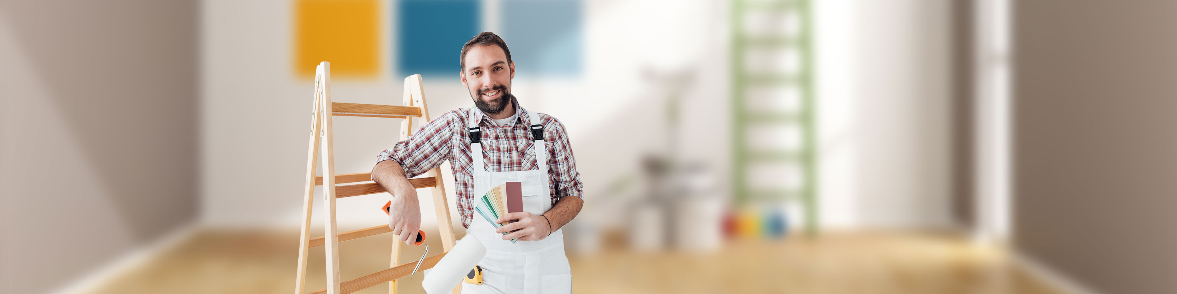 Handwerker in weißer Arbeitskleidung lehnt an einer Leiter, hält Farbmuster und Malerwerkzeug, im Hintergrund ein heller Raum