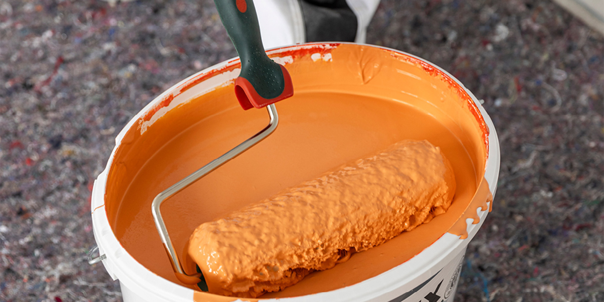 Farbrolle in orangener Farbe im Eimer, Motiv für Vollfarben und Abtönfarben