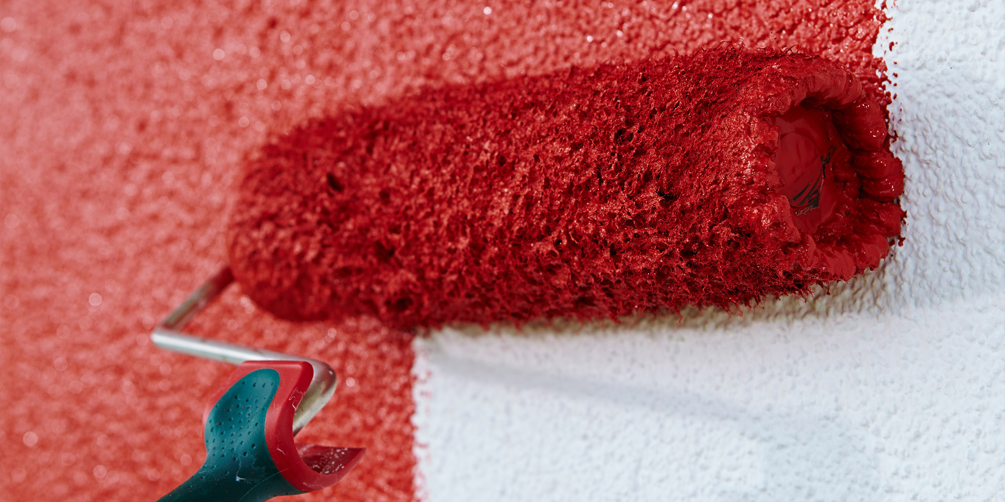 Farbrolle traegt rote Fassadenfarbe auf eine strukturierte Aussenwand auf