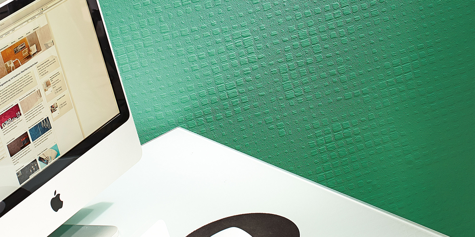 Arbeitsplatz vor gruener Strukturwand. Gewebeoptik als modernes Beispiel