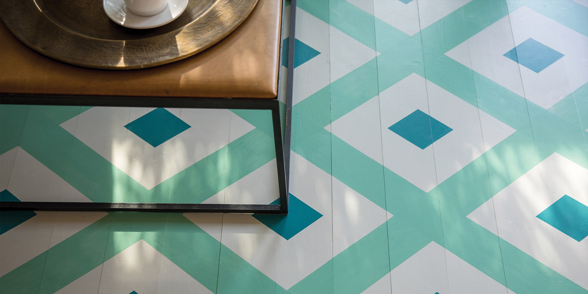 Geometrisch gestrichener Boden in Mint und Türkis mit Rautenmuster, Detail am Tisch