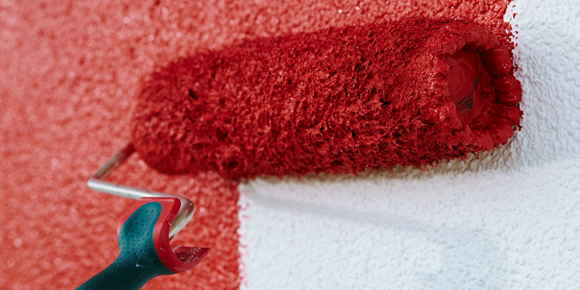 Farbroller bringt rote Fassadenfarbe auf strukturierte Wand, weisser Bereich bleibt sichtbar - Farbwechsel im Anstrich