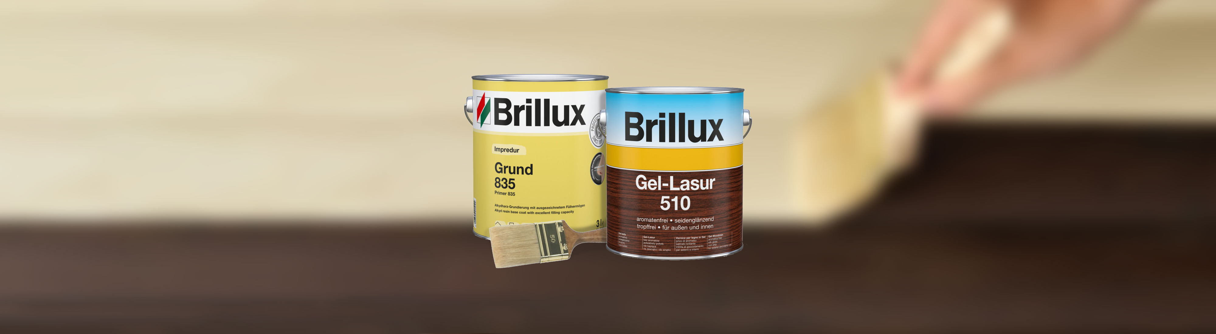 Zwei Dosen Brillux Grundierung und Gel-Lasur mit Pinsel vor unscharfem Holz-Hintergrund