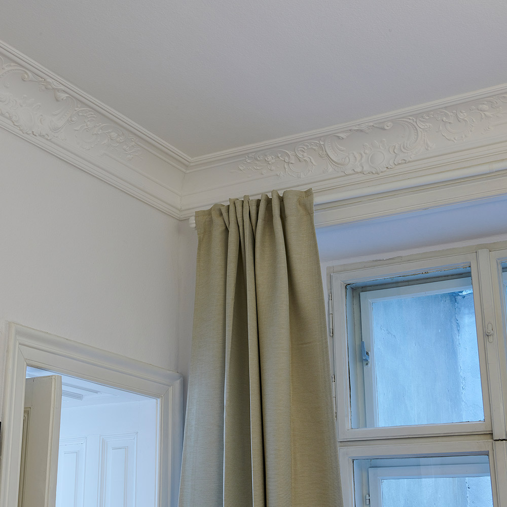 Ein Altbauwohnzimmer mit verzierten Deckenleisten im barocken Stil.