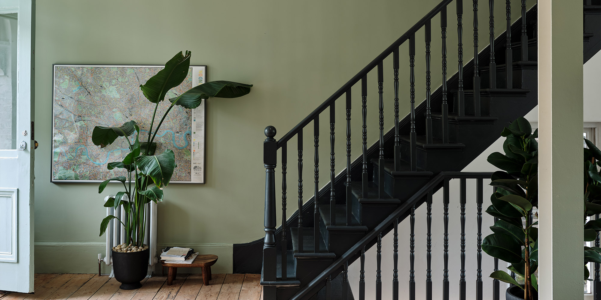 Schwarzes Treppengeländer in Flur mit grüner Wand, Pflanzen und Stadtkarte