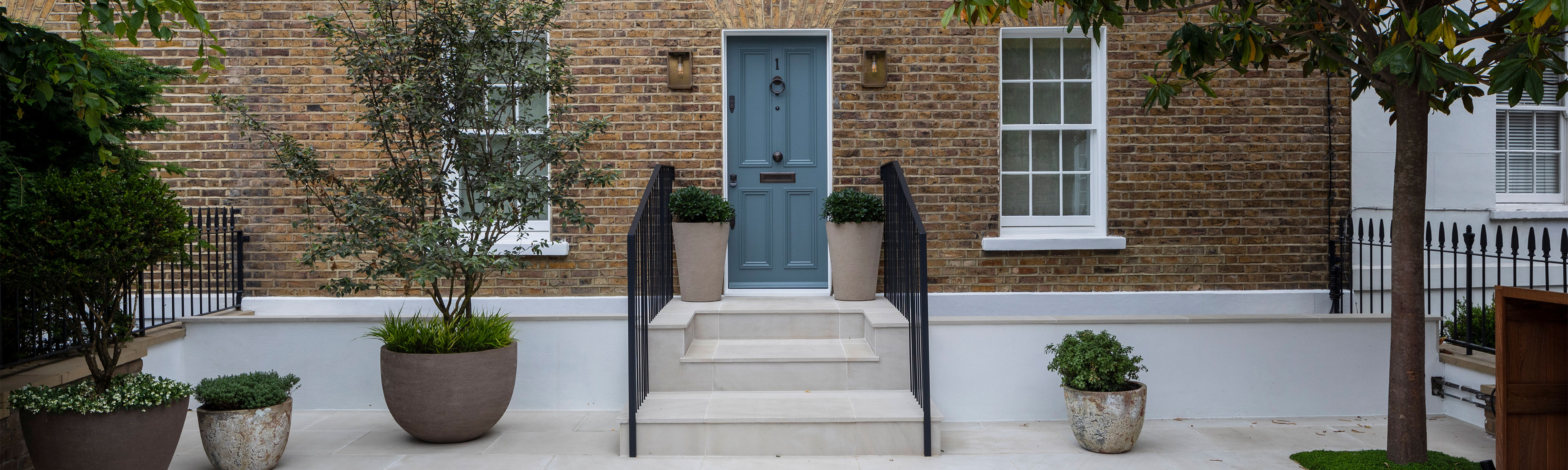 Eingang mit blaugrauer Haustür in Backsteinfassade, Treppe und Pflanzkübel - Headermotiv für Haustüren streichen