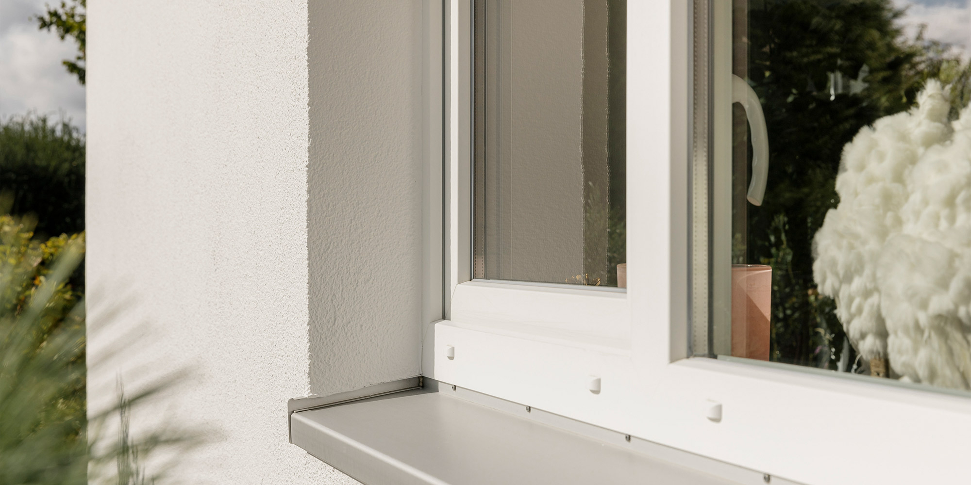 Außenfenster mit weißem Rahmen und grauer Fensterbank an verputzter Fassade