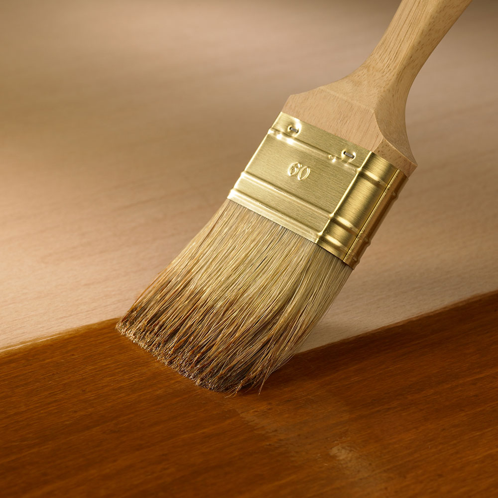 Pinsel trägt Lasur auf eine Holzfläche auf - gleichmäßiger Auftrag beim Haustüren streichen