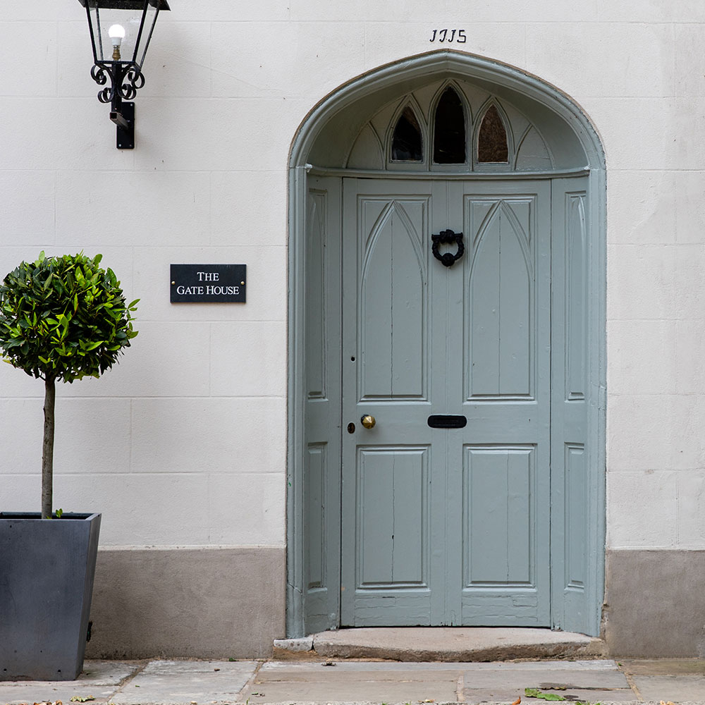 Hellgraue Holzhaustür mit Rundbogen in weißer Fassade, Wandlaterne und Kübelpflanze - Inspiration zum Streichen