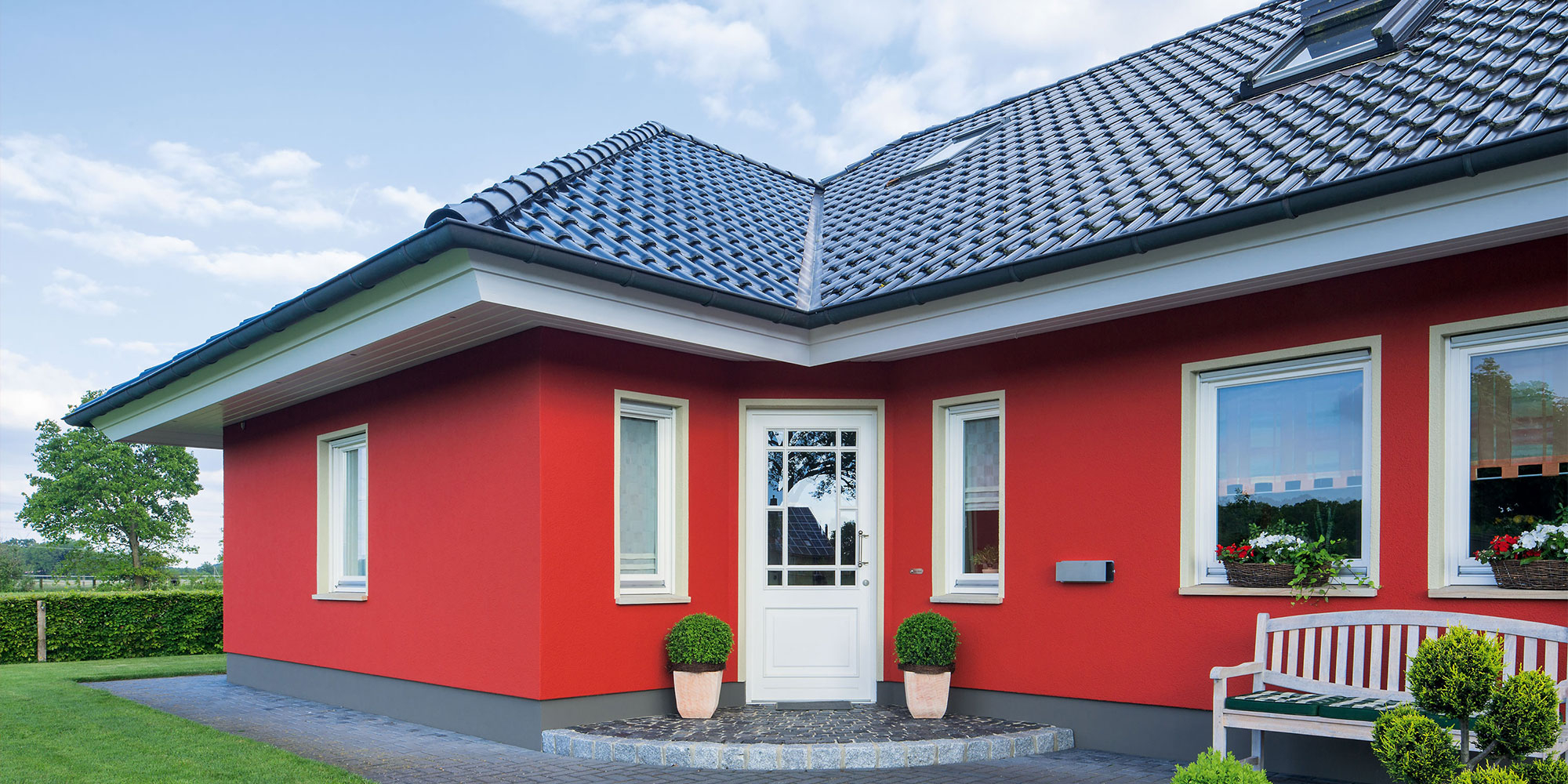 Einfamilienhaus mit roter Fassade, weissen Fenstern und dunklem Dach - Beispiel fuer Fassadenfarbe und Schutz