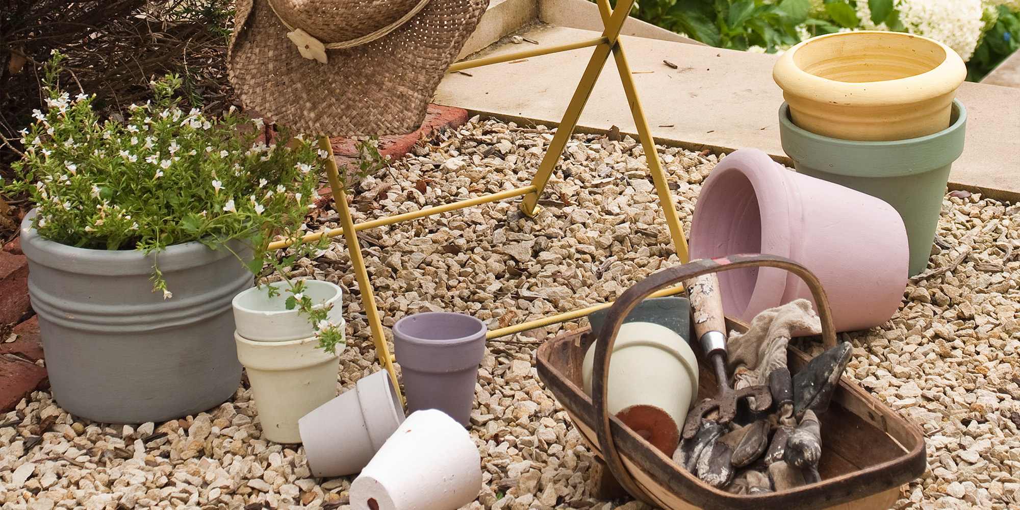 Pastellfarbene Blumentöpfe und Gartengeräte auf Kies als DIY Farbidee
