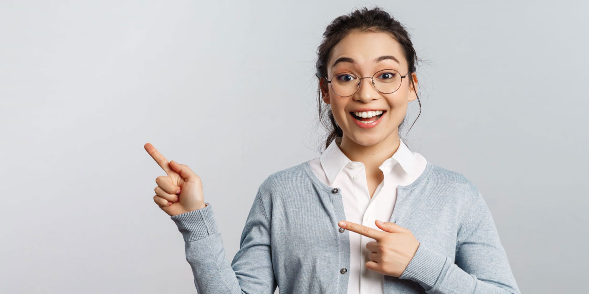 Junge Frau mit Brille lächelt und zeigt mit den Fingern auf eine freie Fläche, bereit Tipps zu geben