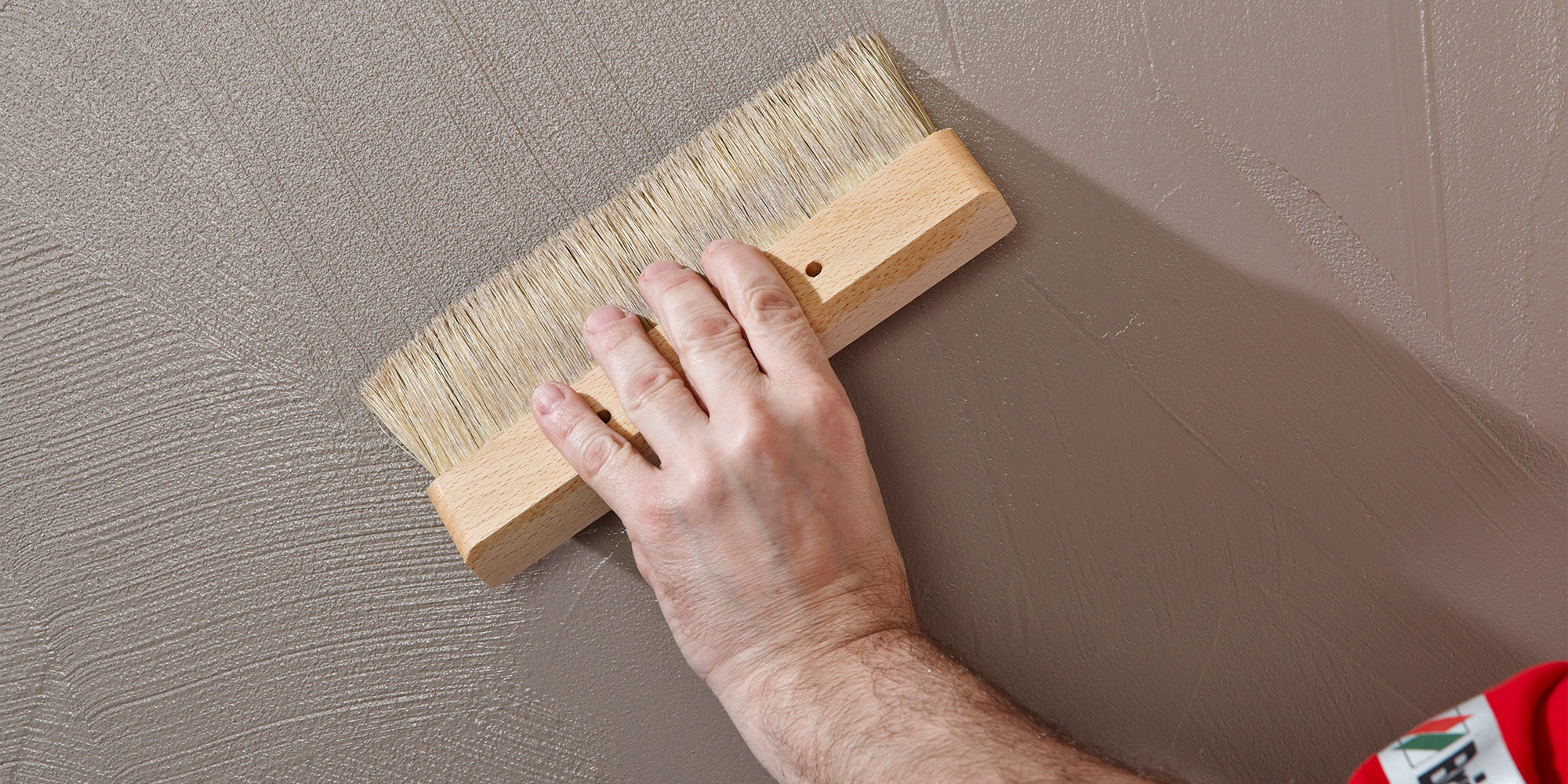 Hand fuehrt breiten Pinsel ueber die Wand, Beispiel fuer Werkzeuge zum Streichen und Beschichten