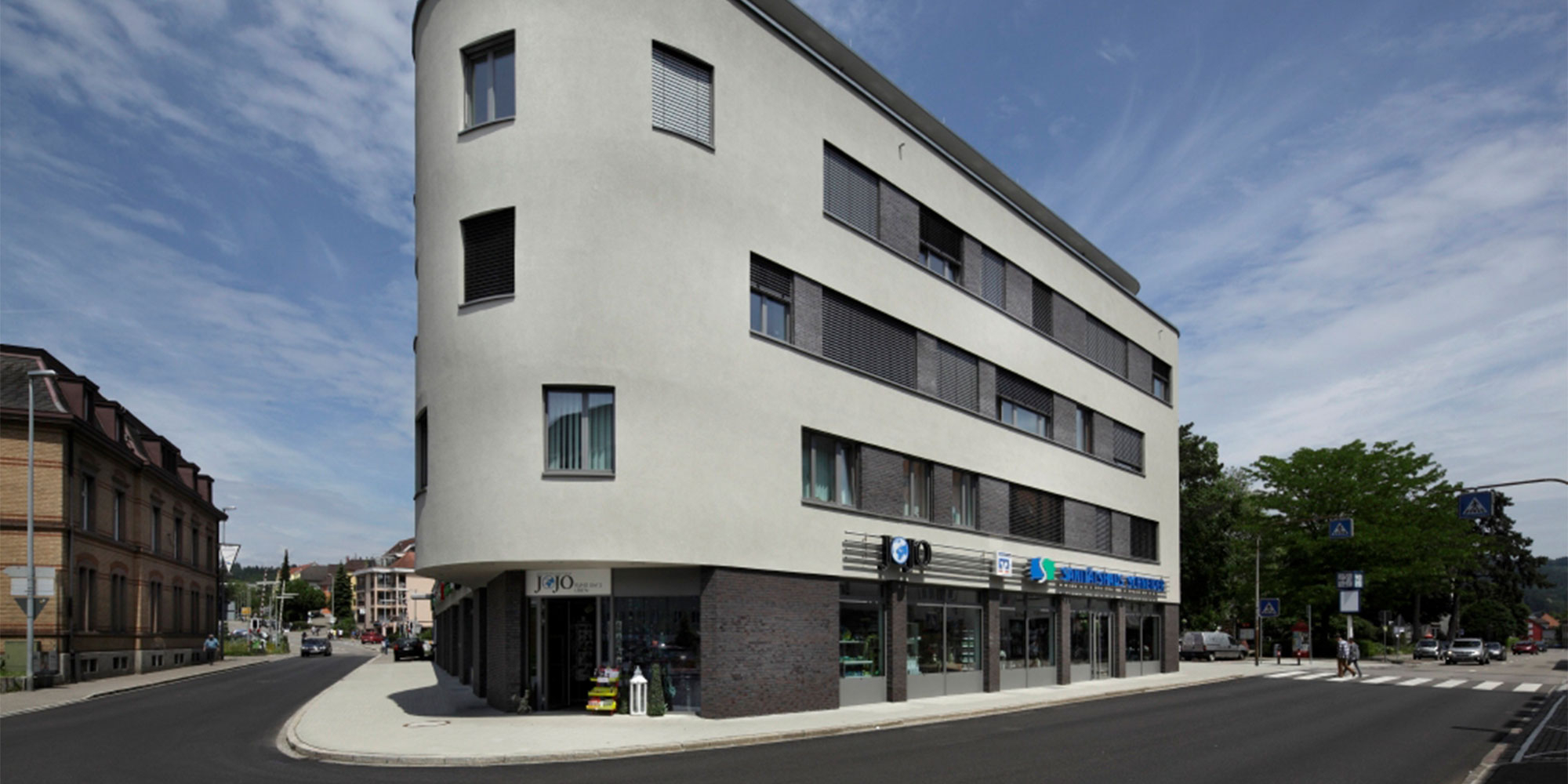 Modernes Gebäude mit heller Rausanputz Fassade und großen Fensterflächen in der Straßenansicht